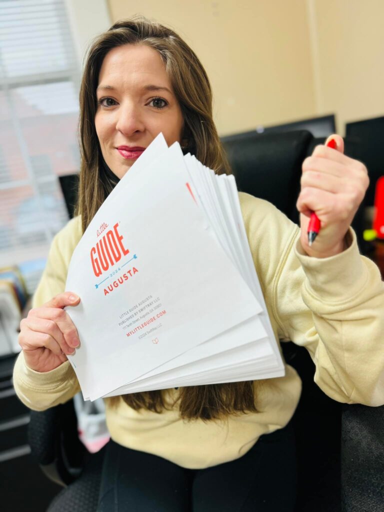 Jessica Baskette holding Rough draft of Little Guide Augusta with a red pen.